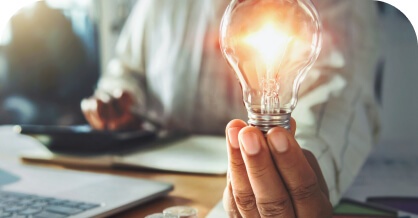 Hand holding a glowing lightbulb over a desk