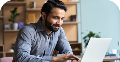 Man in a gray shirt smiling at a laptop in an office