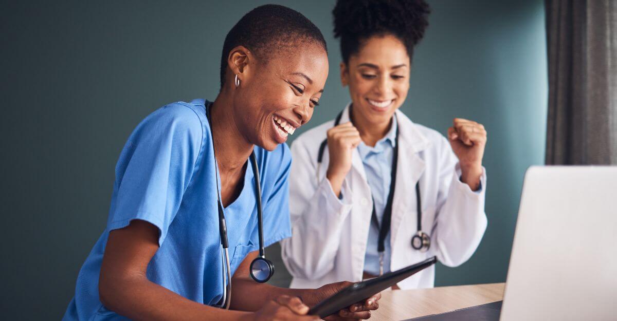 Two front-line healthcare workers celebrate while reviewing pay or performance updates on a digital device, representing how modern compensation management empowers and supports front-line teams.