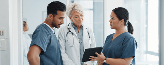 Three healthcare workers in scrubs talking in a hospital