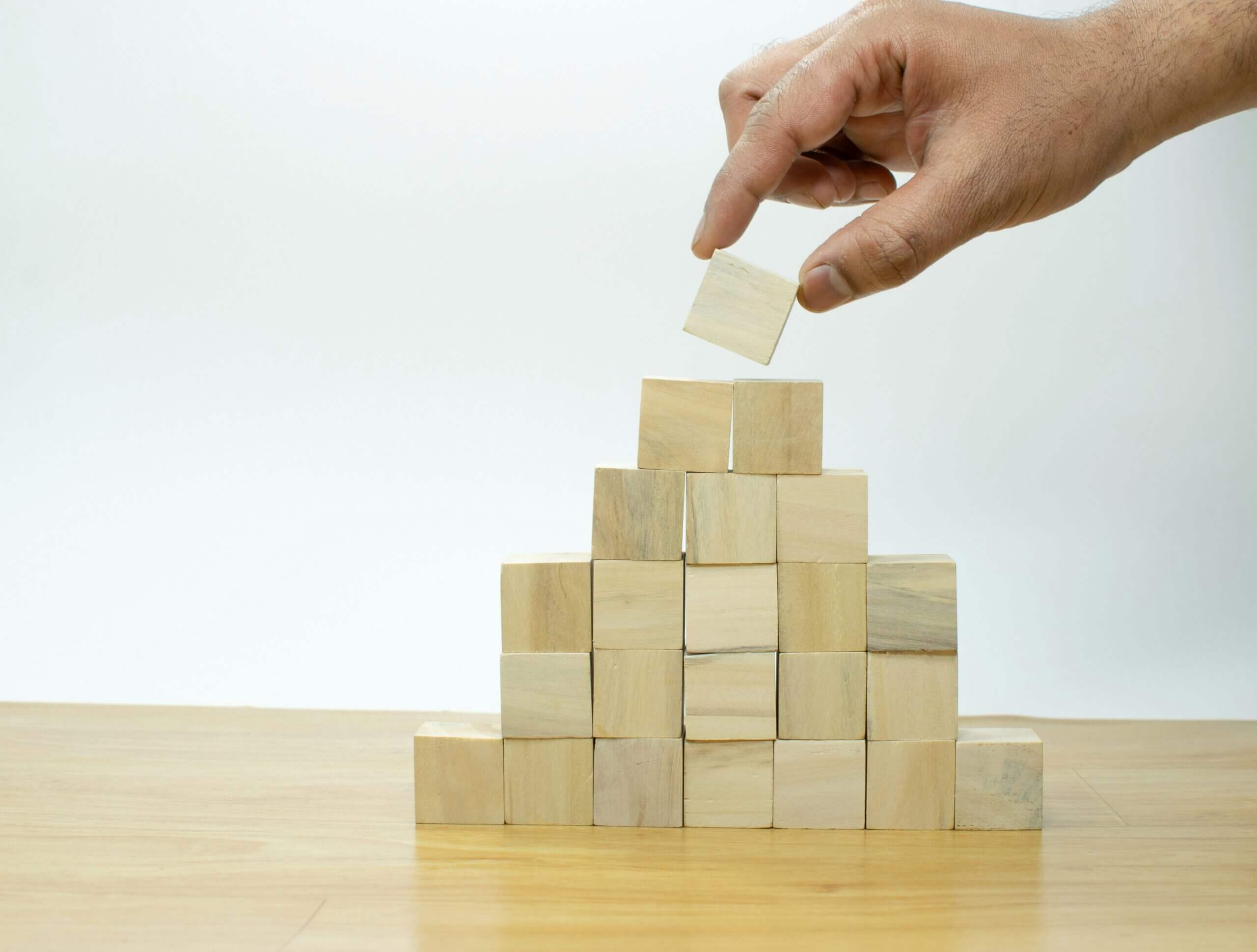Hand stacking wooden blocks into a pyramid, symbolizing growth