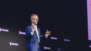Man in a blue suit presenting on stage at a conference
