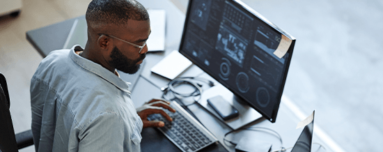 Man wearing headphones working at a desk with multiple data monitors