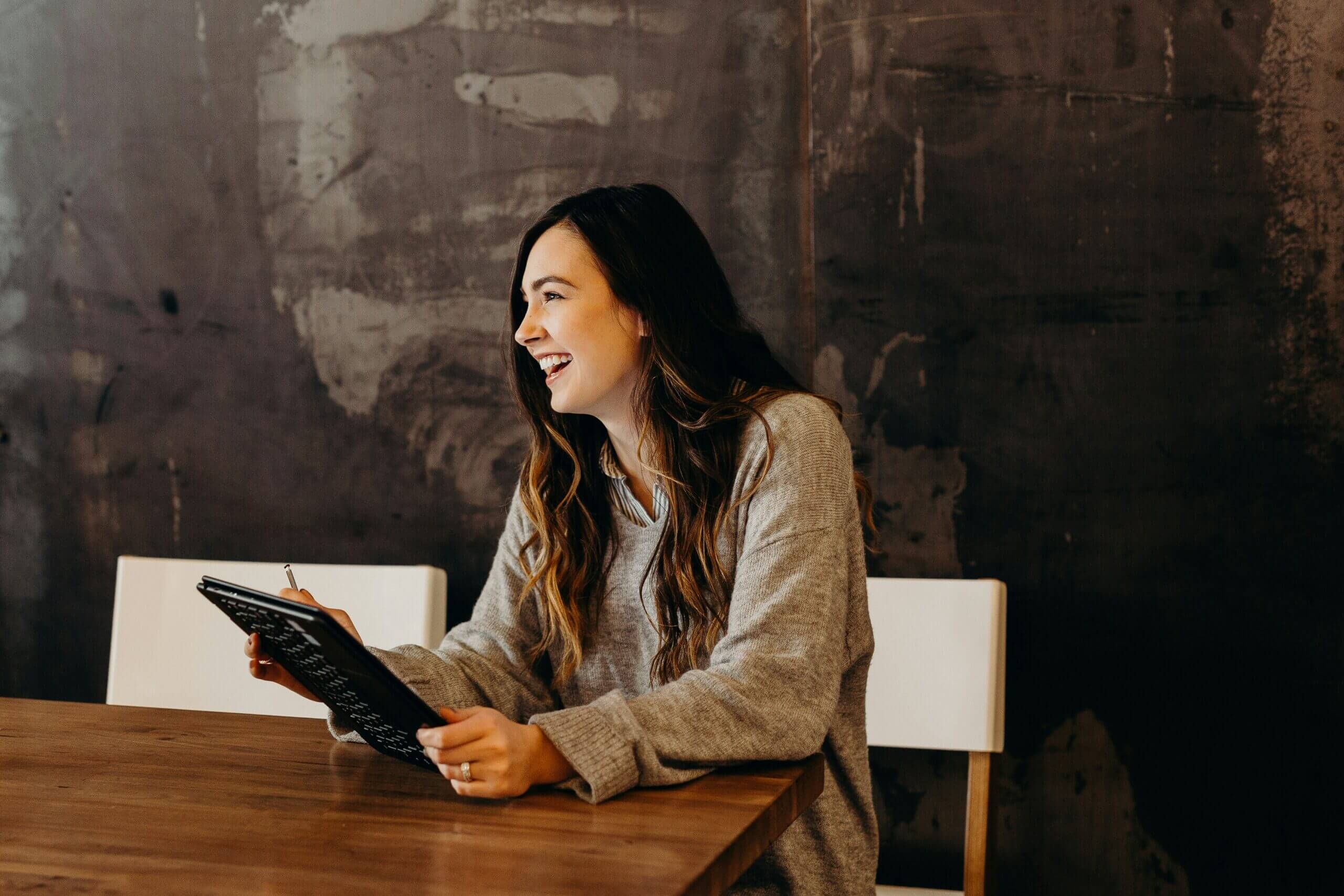 Smiling woman holding a tablet while seated at a table