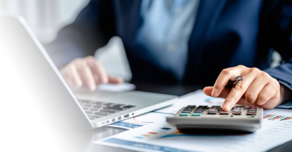 Business professional using a calculator and laptop to analyze financial charts, symbolizing how HR leaders calculate the ROI of compensation software for global enterprises.