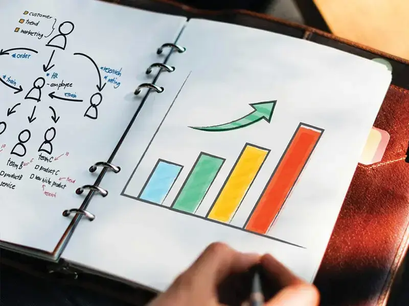 Hand drawing a bar chart with an upward arrow in a notebook
