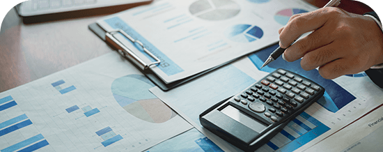 Hand using a calculator over financial charts and documents