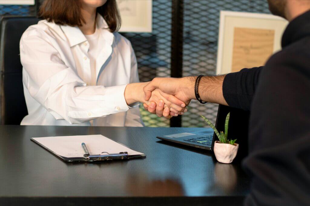 Two professionals shaking hands across a desk during a business meeting